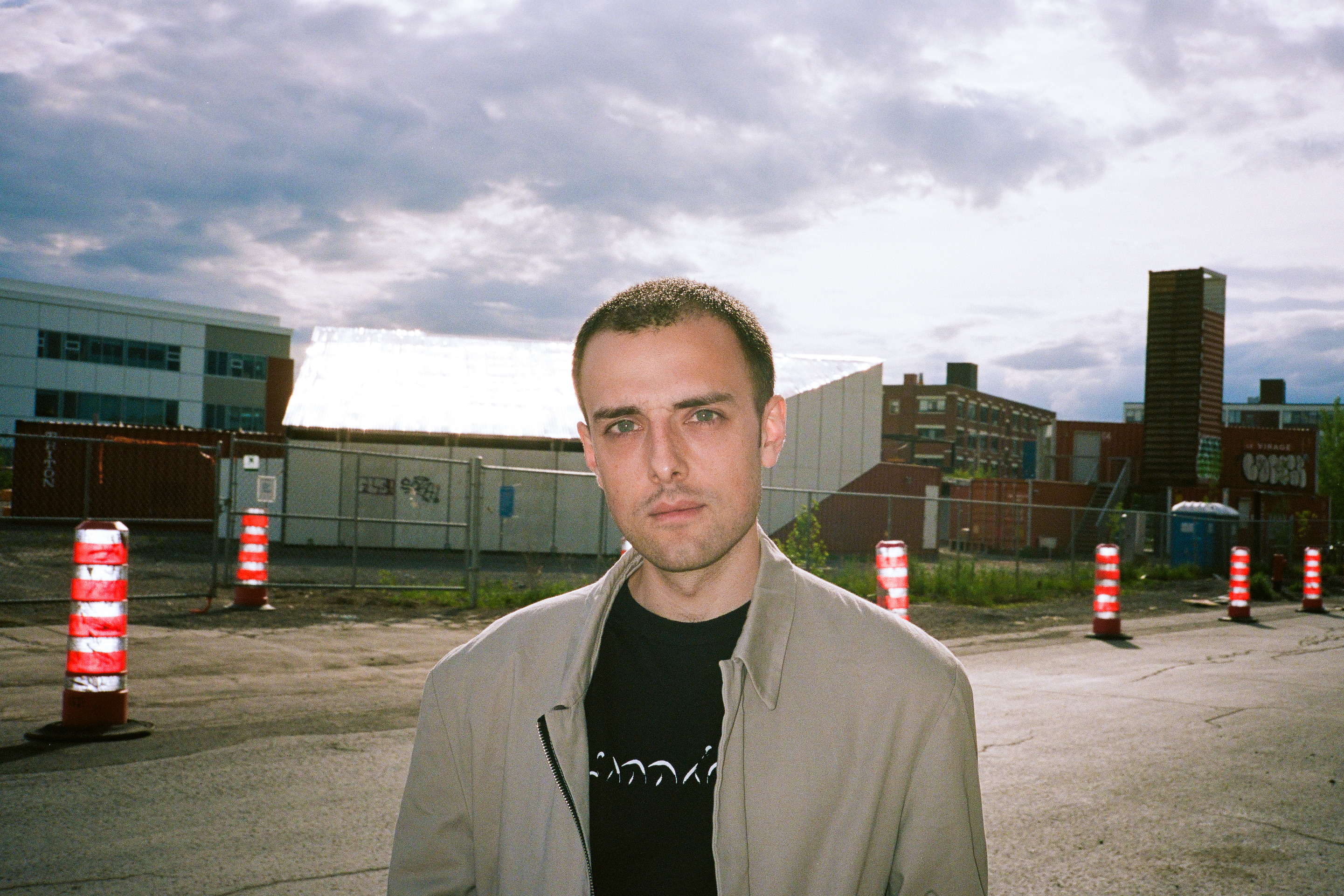 Simon Chioini en manteau devant des cônes orange et un ciel nuageux. Crédit photo : Ilyaa Ghafouri.